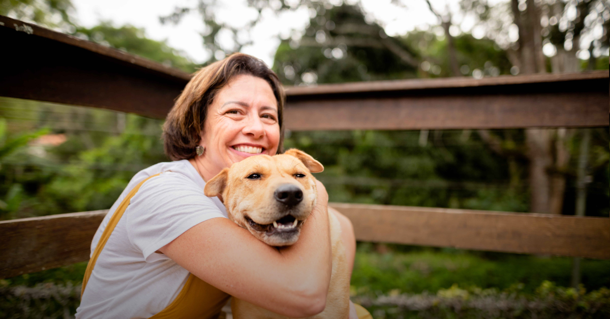 A woman smiles while cuddling a dog outside